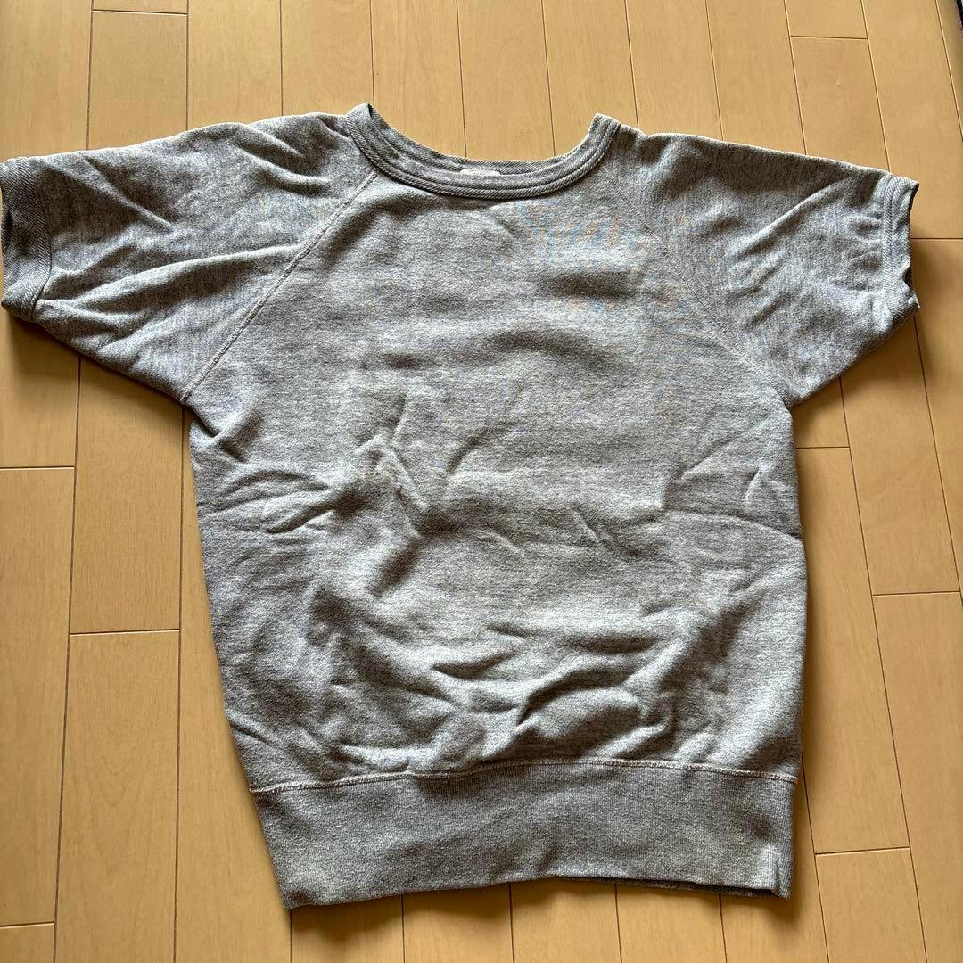 Grey short-sleeve sweatshirt laid flat on a wooden floor.