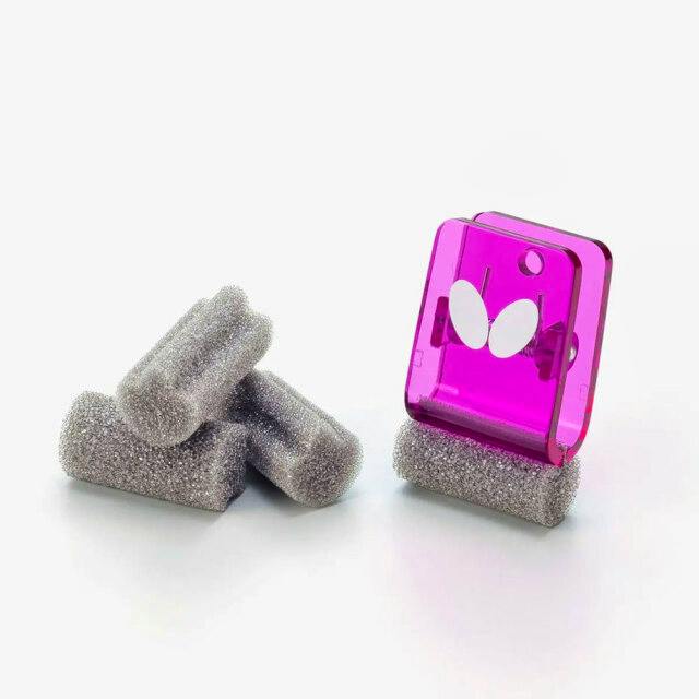 Several small gray sponge pieces shown next to a translucent pink clip with a white butterfly logo on a white background.