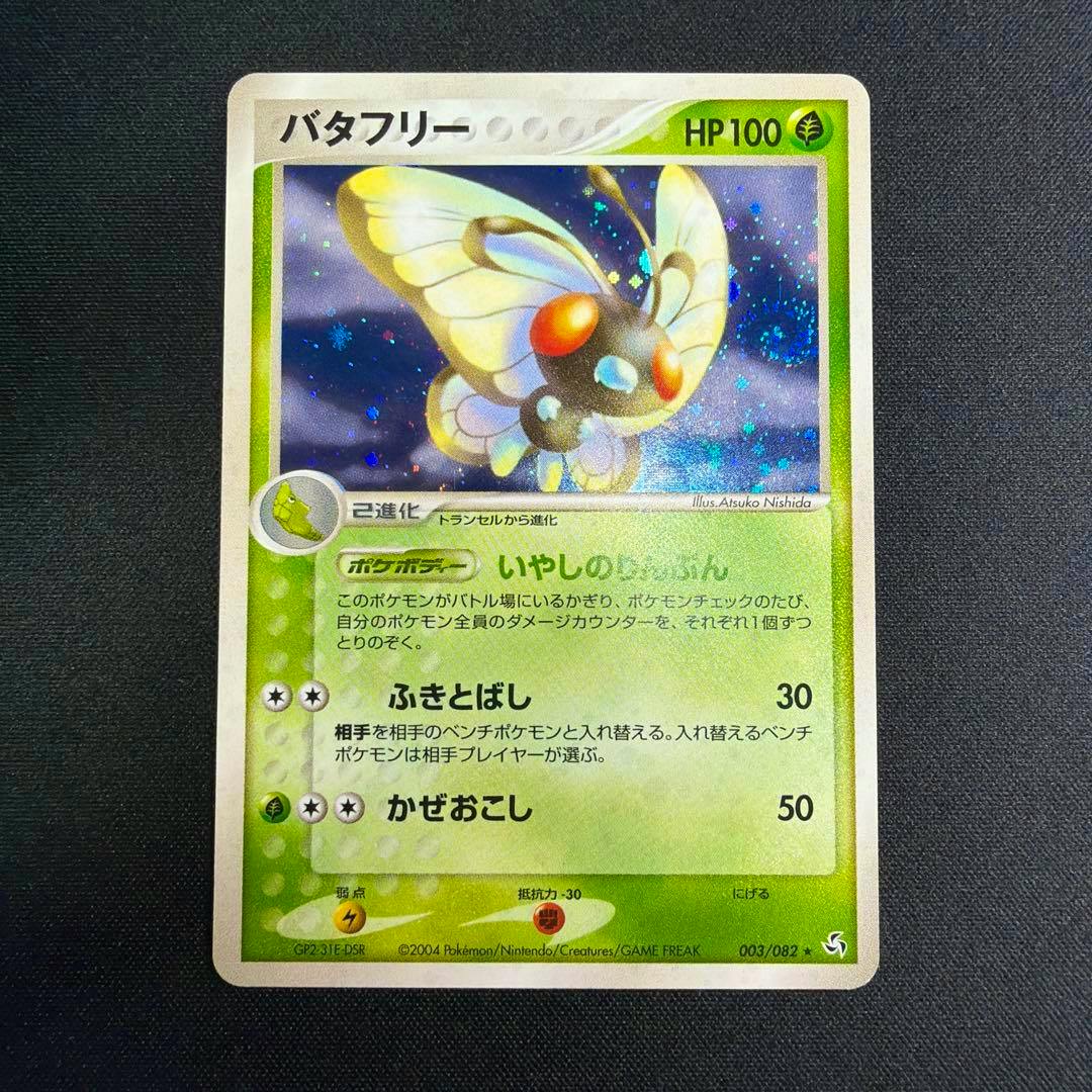A holographic Japanese Butterfree trading card (HP100) shown face-up on a dark textured background.