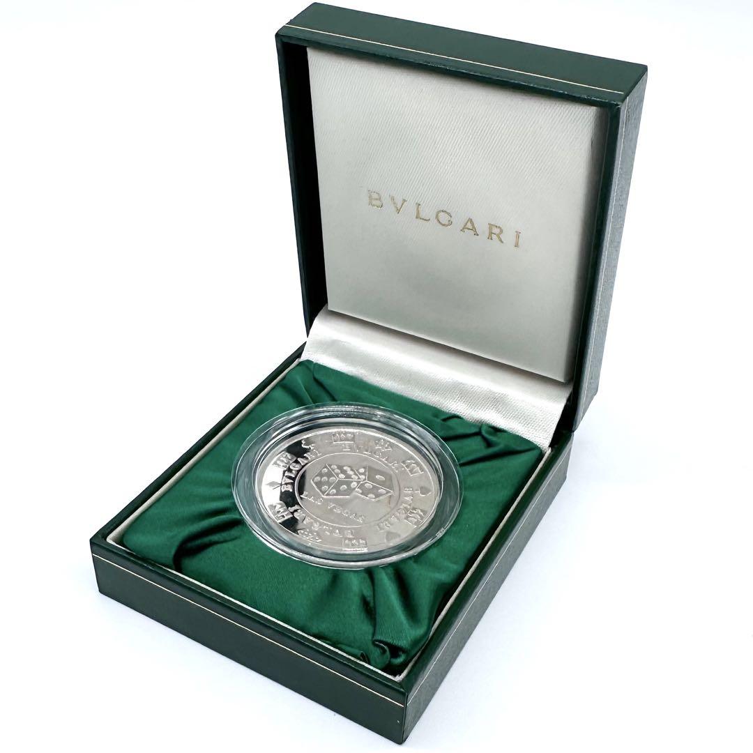 A silver BVLGARI Las Vegas casino coin in a clear capsule displayed inside a green BVLGARI presentation box with satin lining.