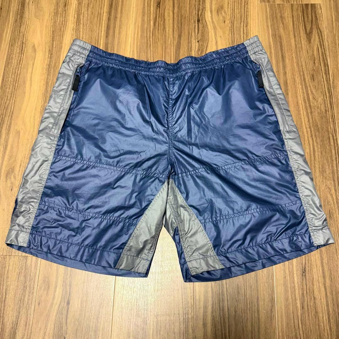 Front view of C.E CAVEMPT navy and gray warm up shorts laid flat on a wood floor.
