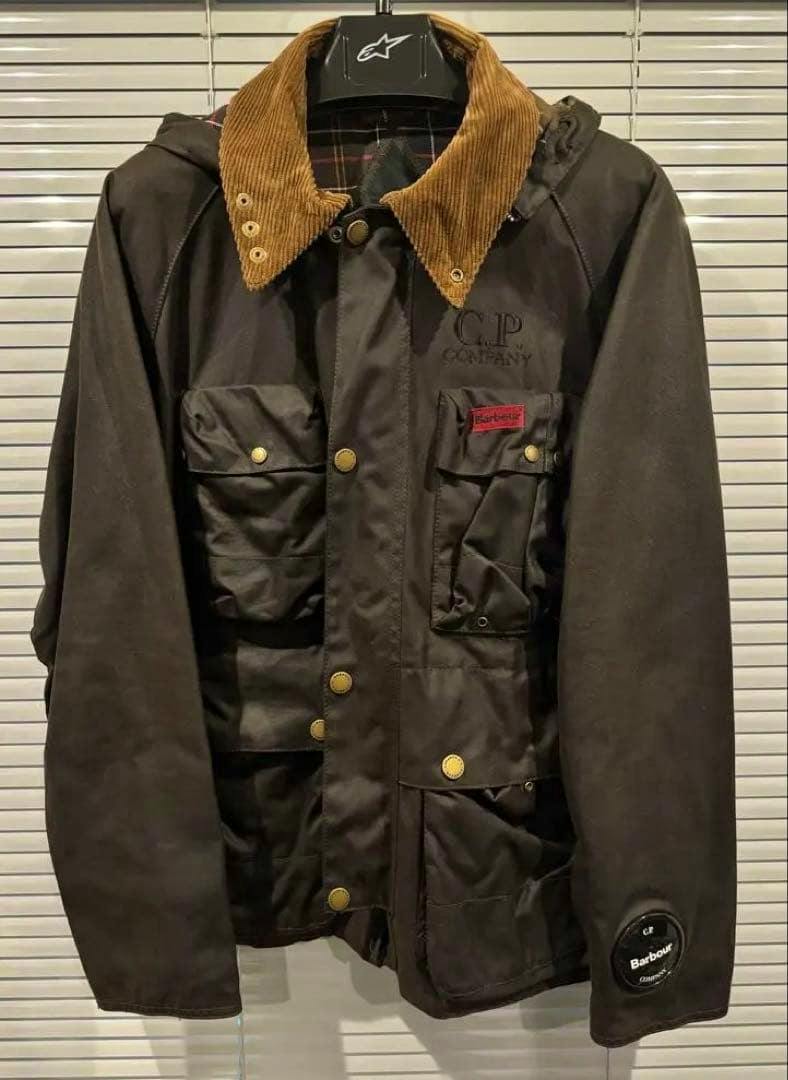 Front view of the C.P. COMPANY x Barbour waxed men's jacket (size L) showing a brown corduroy collar, multiple flap pockets, snap buttons, and branded patches.