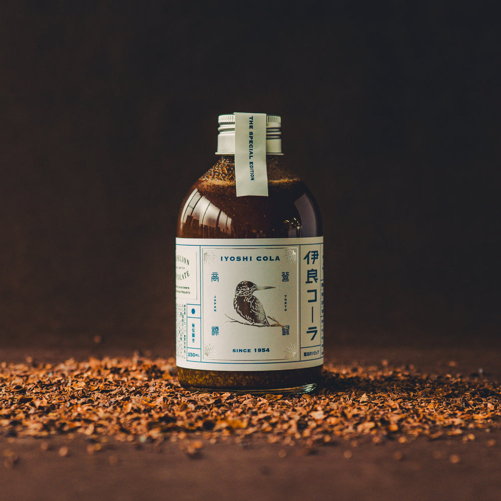 Front view of the 250ml bottled soda drink with a white label featuring a bird illustration, sitting on a surface scattered with small brown pieces.