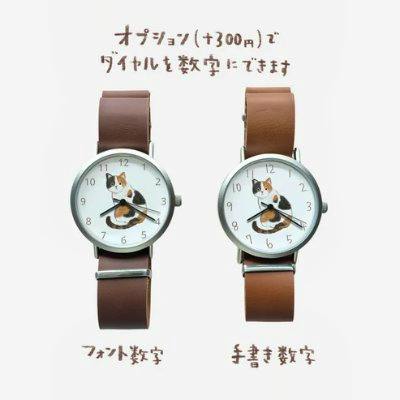 Front view of the watch with a metal case, brown leather strap, and a calico cat illustration on the dial.