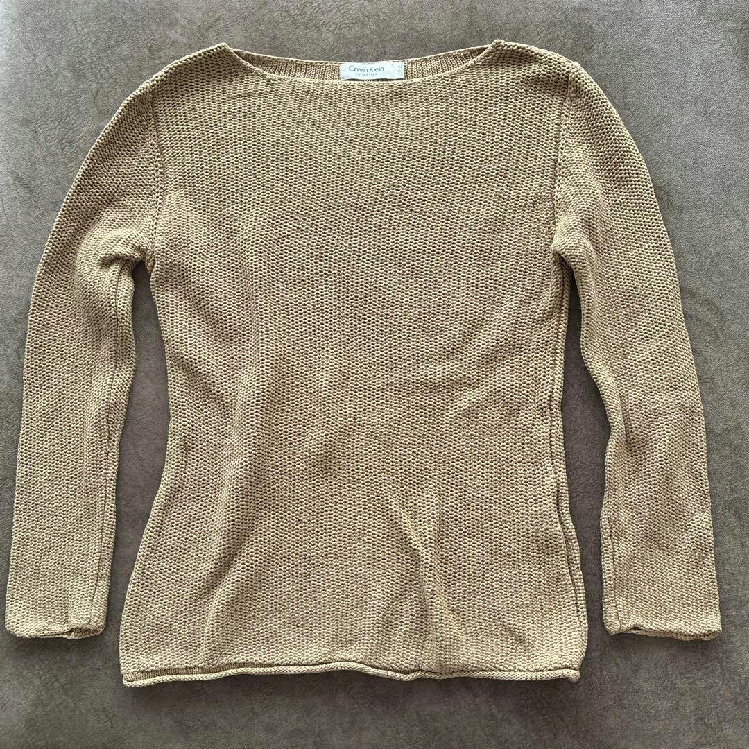 Beige long-sleeve crew-neck knit sweater laid flat with a visible Calvin Klein label.