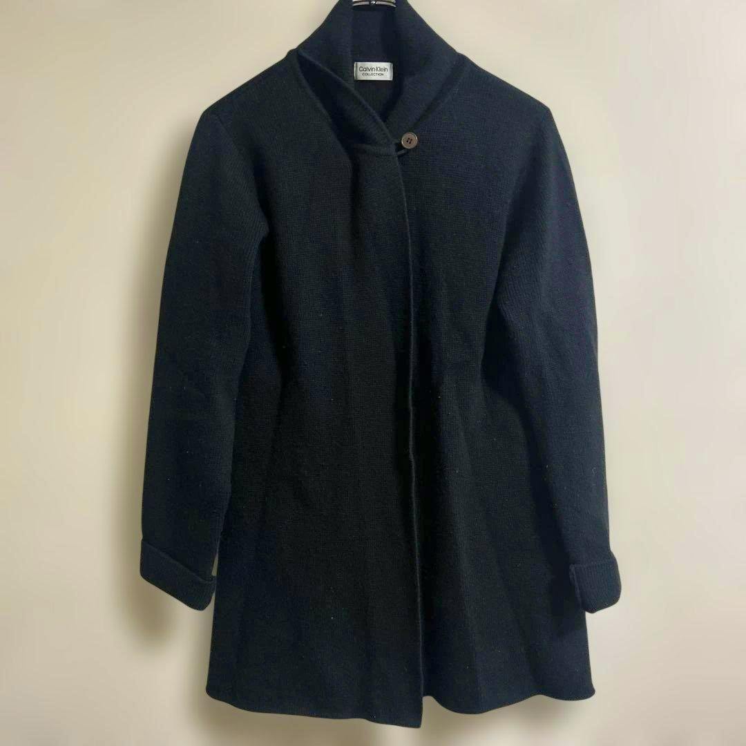 A black Calvin Klein Collection long coat hanging on a hanger against a plain light background.