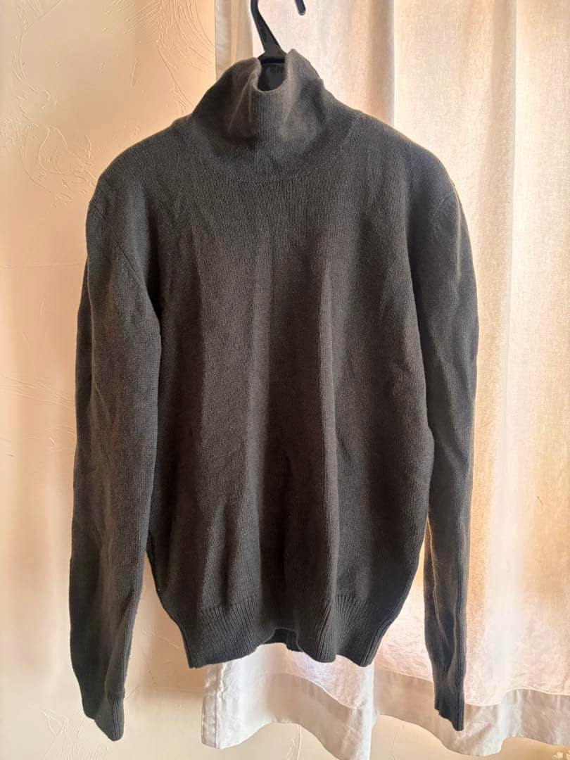 Calvin Klein Collection turtleneck knit sweater hanging on a hanger against a curtain.