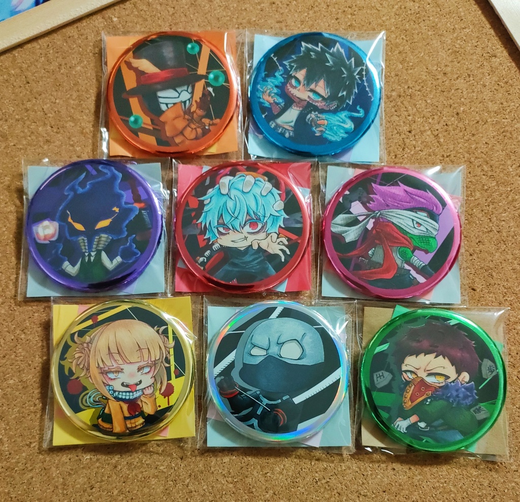 Nine round can badges with colorful anime-style character designs, each in a clear plastic sleeve, arranged on a corkboard.