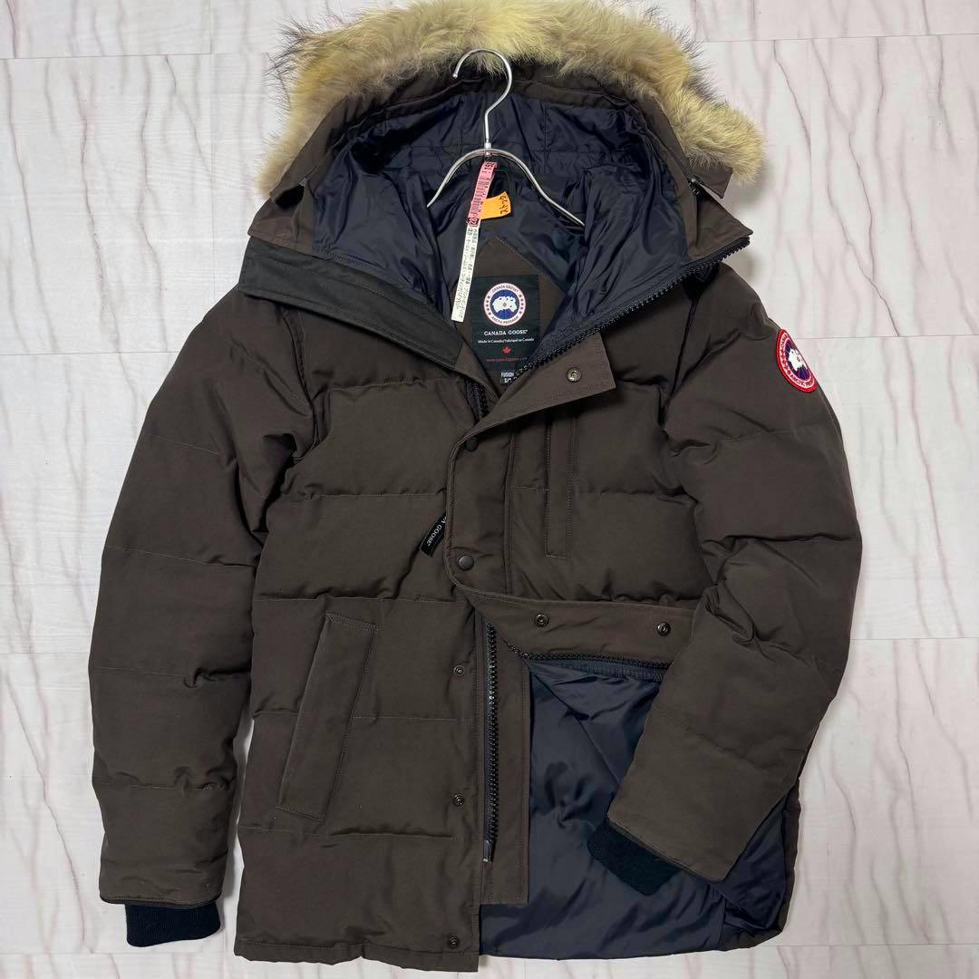 Brown Canada Goose Carson parka jacket laid flat showing the fur-trimmed hood, front zipper, and logo patch.