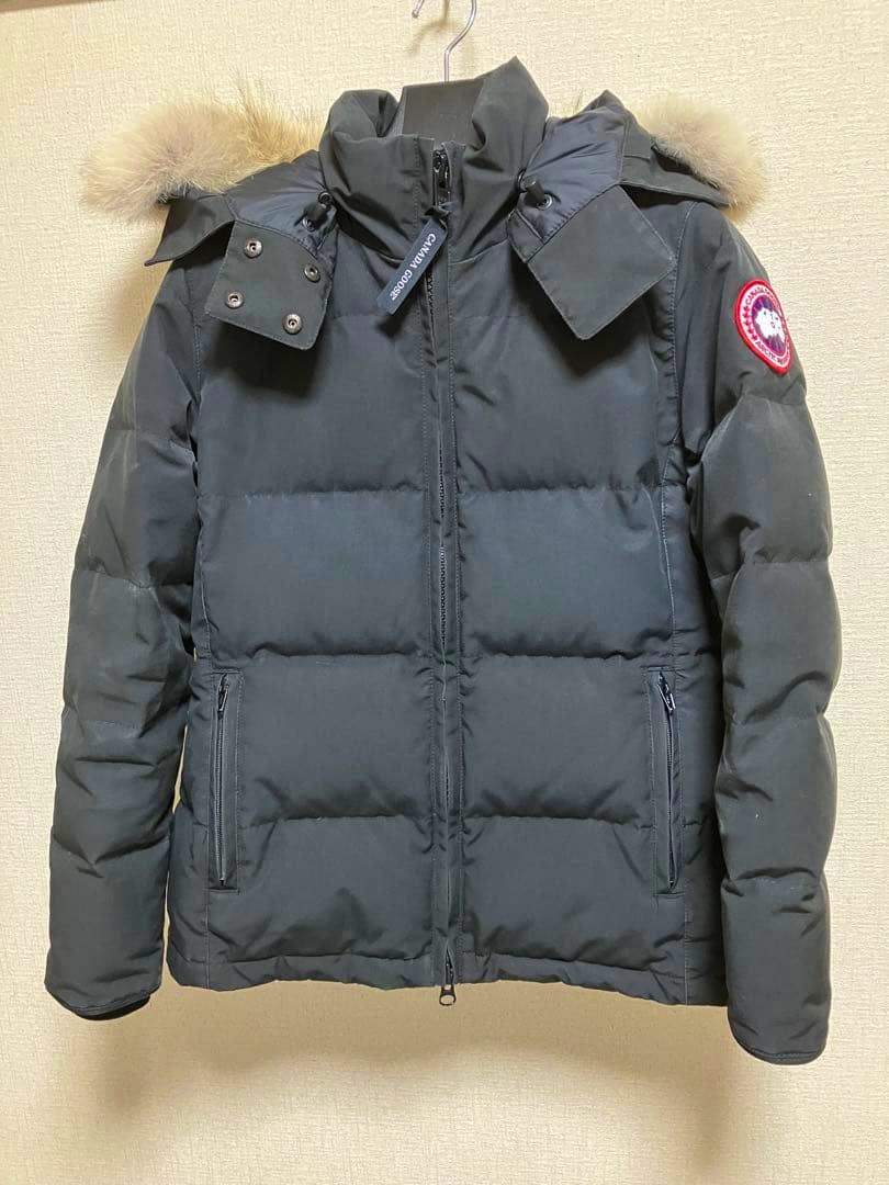 Front view of a black Canada Goose Chelsea parka hanging on a hanger, showing the fur-trimmed hood and sleeve logo.