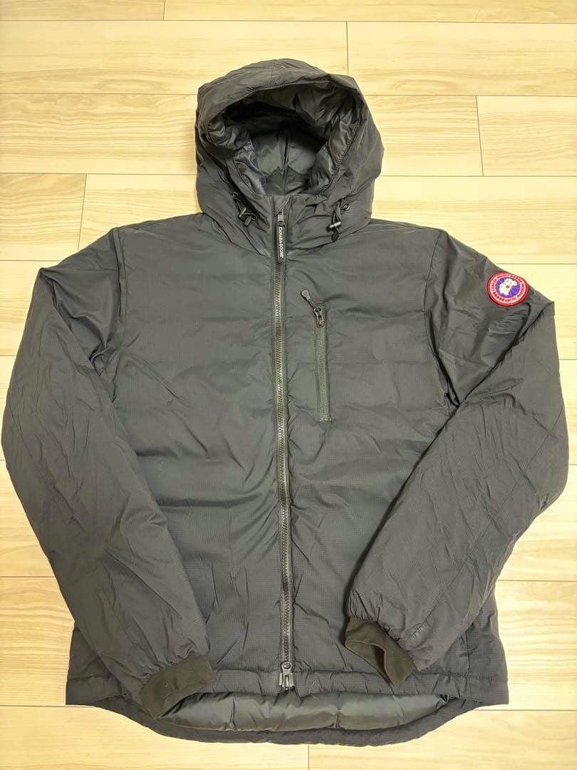 Black Canada Goose Lodge Hoody jacket laid flat on a wooden floor showing the front, hood, and sleeve patch.
