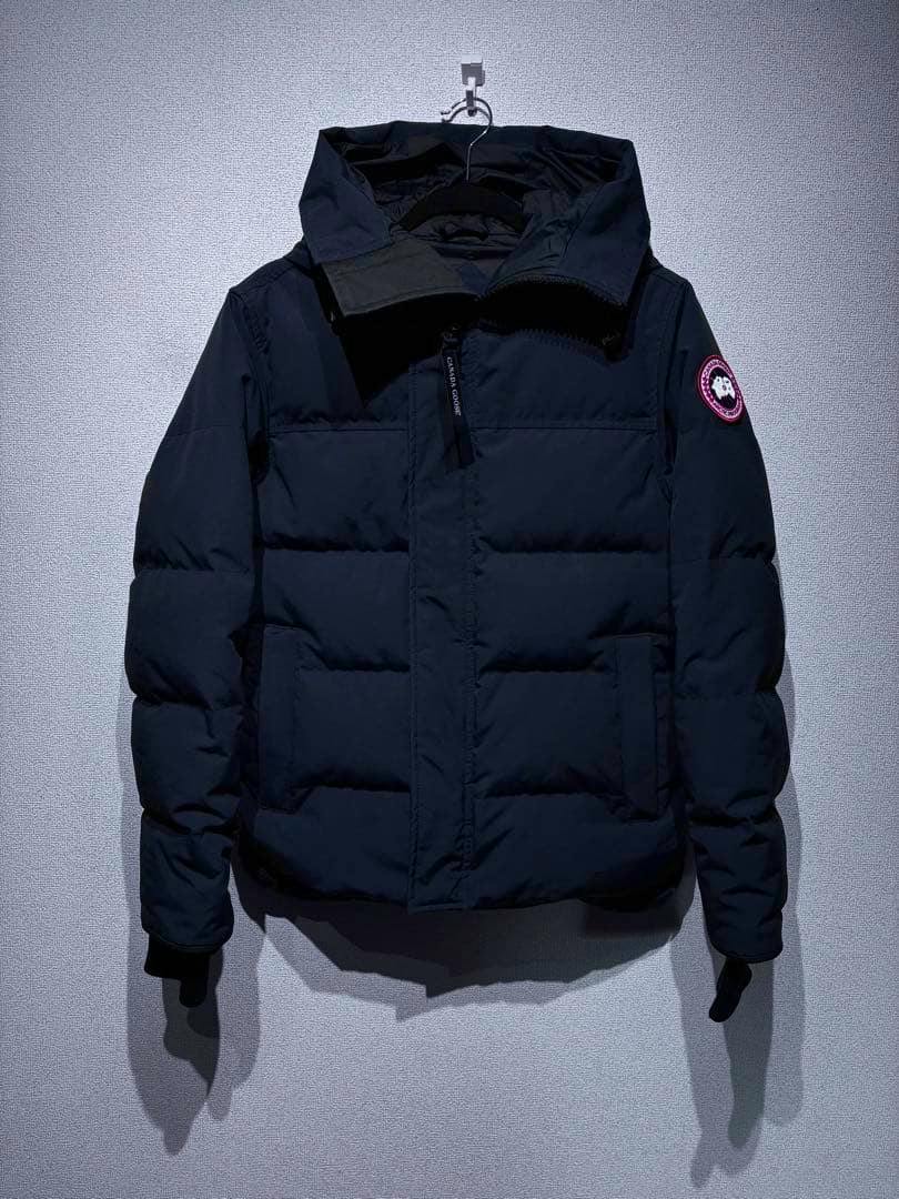 Front view of a dark Canada Goose men's down jacket hanging on a hook with the sleeve logo patch visible.