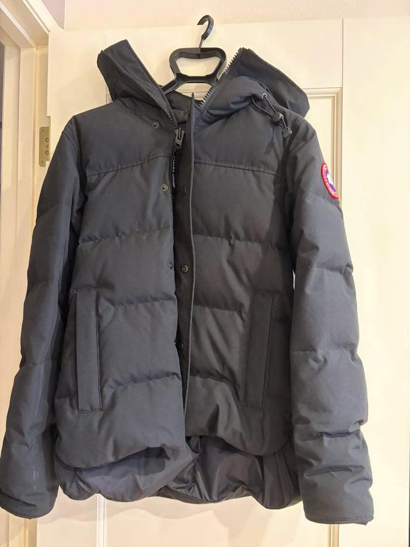 Canada Goose men's down jacket hanging on a hanger, front view with hood and pockets.