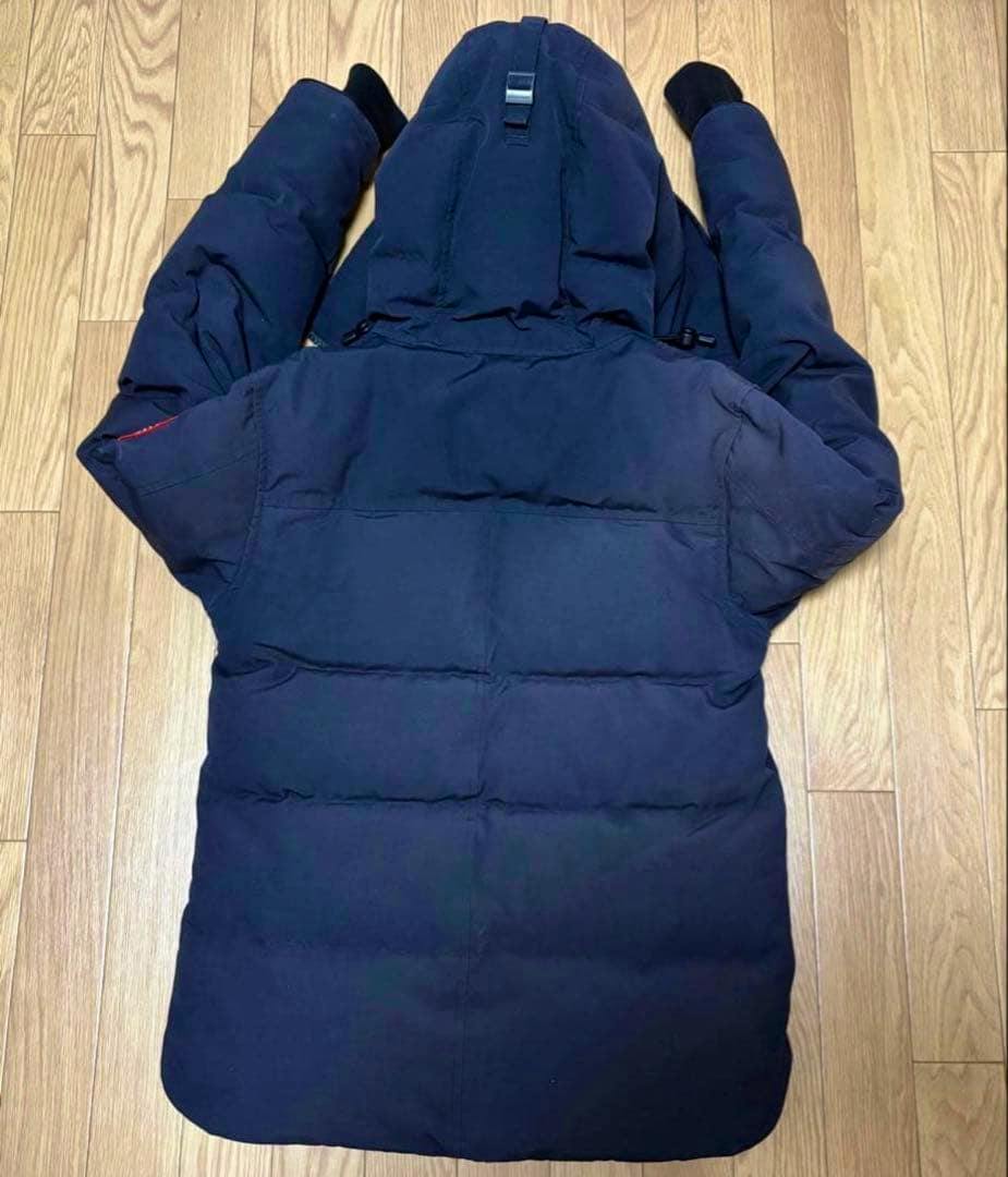Back view of a men's Canada Goose down jacket with hood laid flat on a wooden floor.