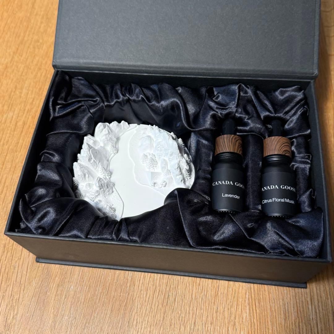 A white Canada Goose aroma diffuser stone in a black satin-lined gift box alongside two small Canada Goose bottles.
