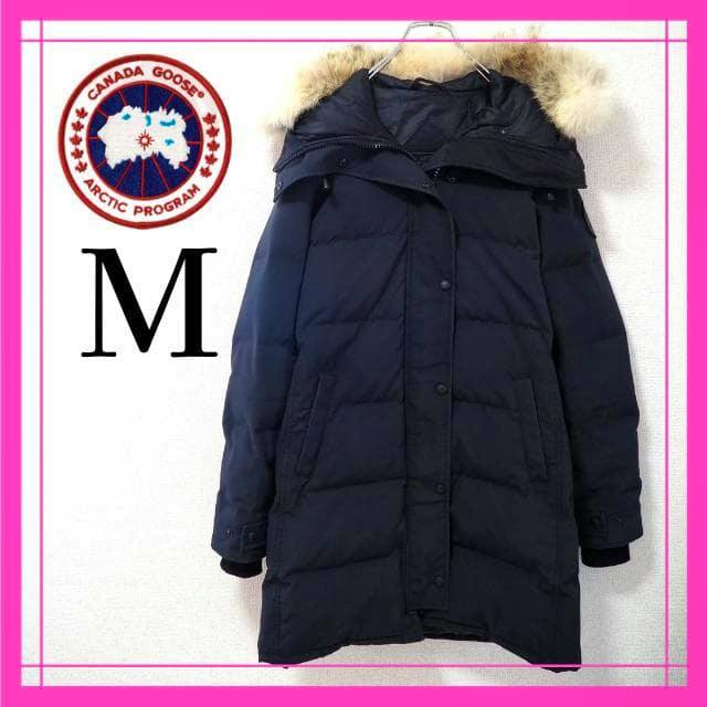 Front view of a navy men's jacket (CANADA GOOSE Shelburne) with a fur-trimmed hood hanging on a hanger.