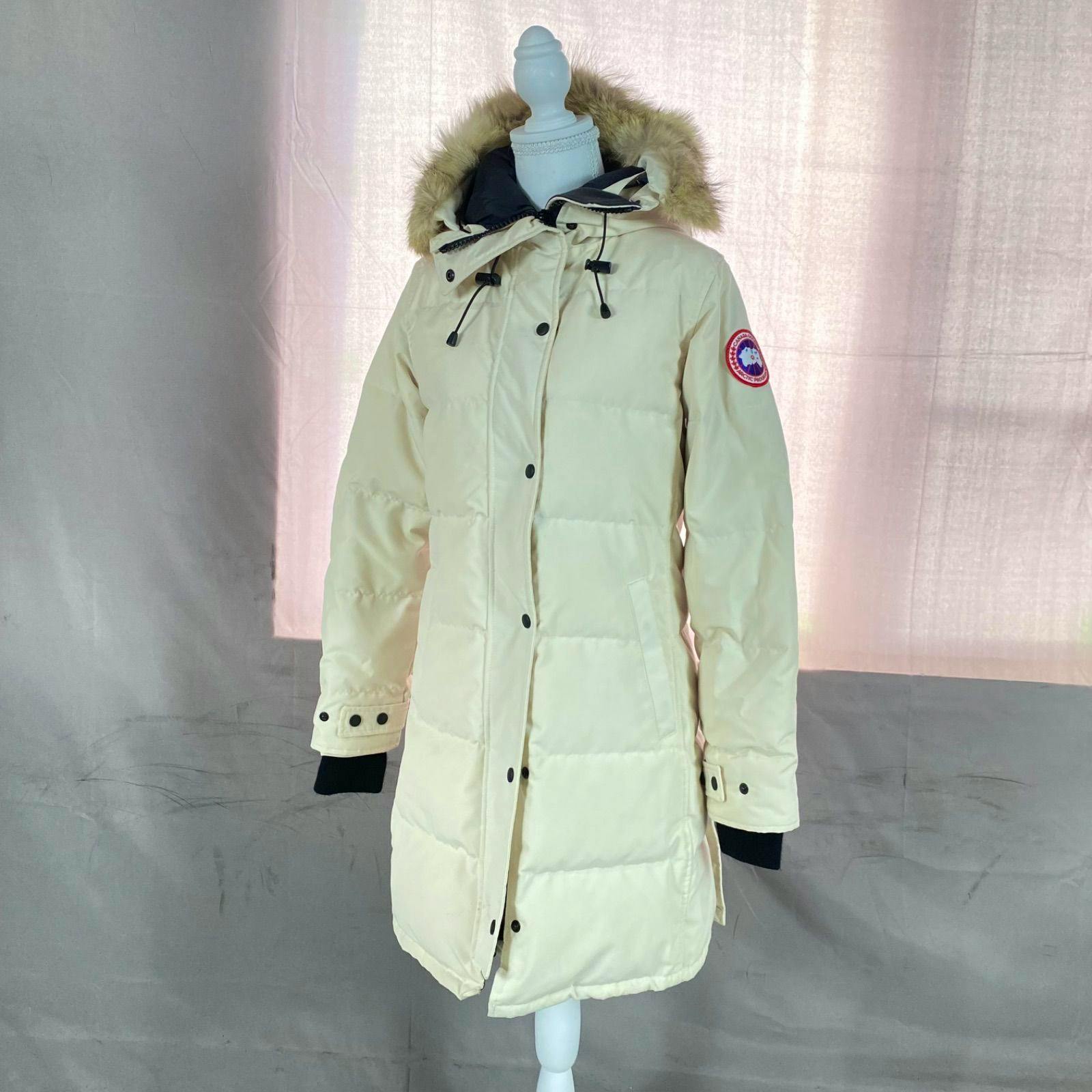 Ivory Canada Goose Shelburne parka with a coyote-fur trimmed hood displayed on a mannequin against a fabric backdrop.