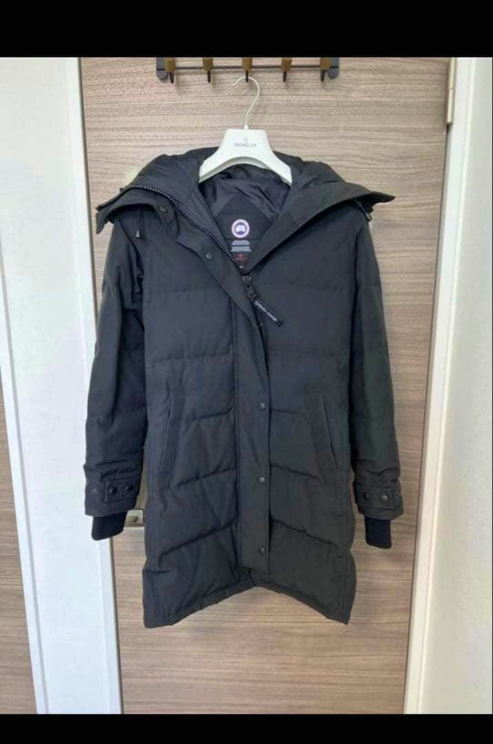 Front view of a black Canada Goose Shelburne women's parka hanging on a hanger against a wooden door.