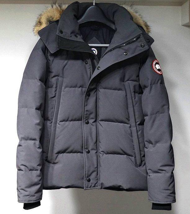 Front view of a gray CANADA GOOSE Wyndham Parka men's down jacket with fur-trimmed hood hanging on a hanger.
