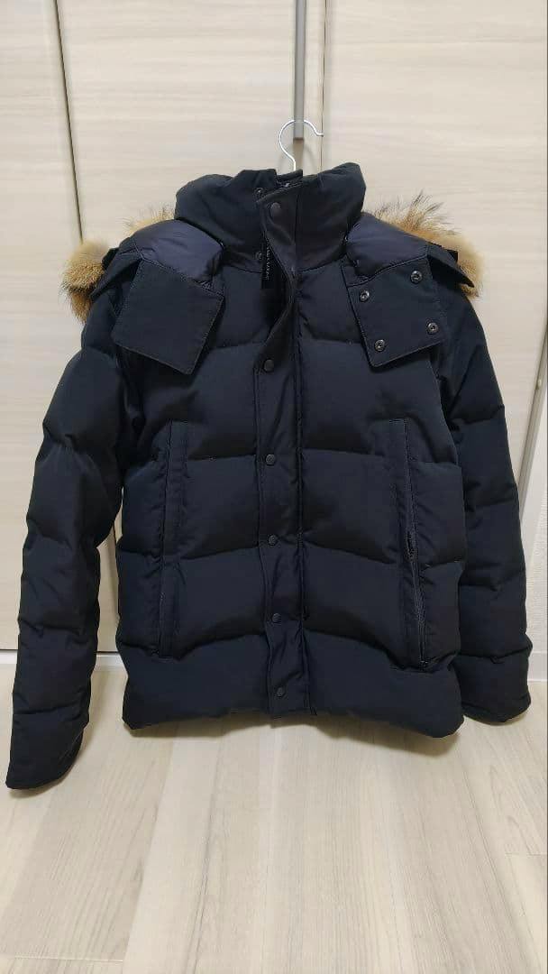 Front view of the black Canada Goose Wyndham parka (men's down jacket) on a hanger showing front pockets and a fur-trimmed hood.