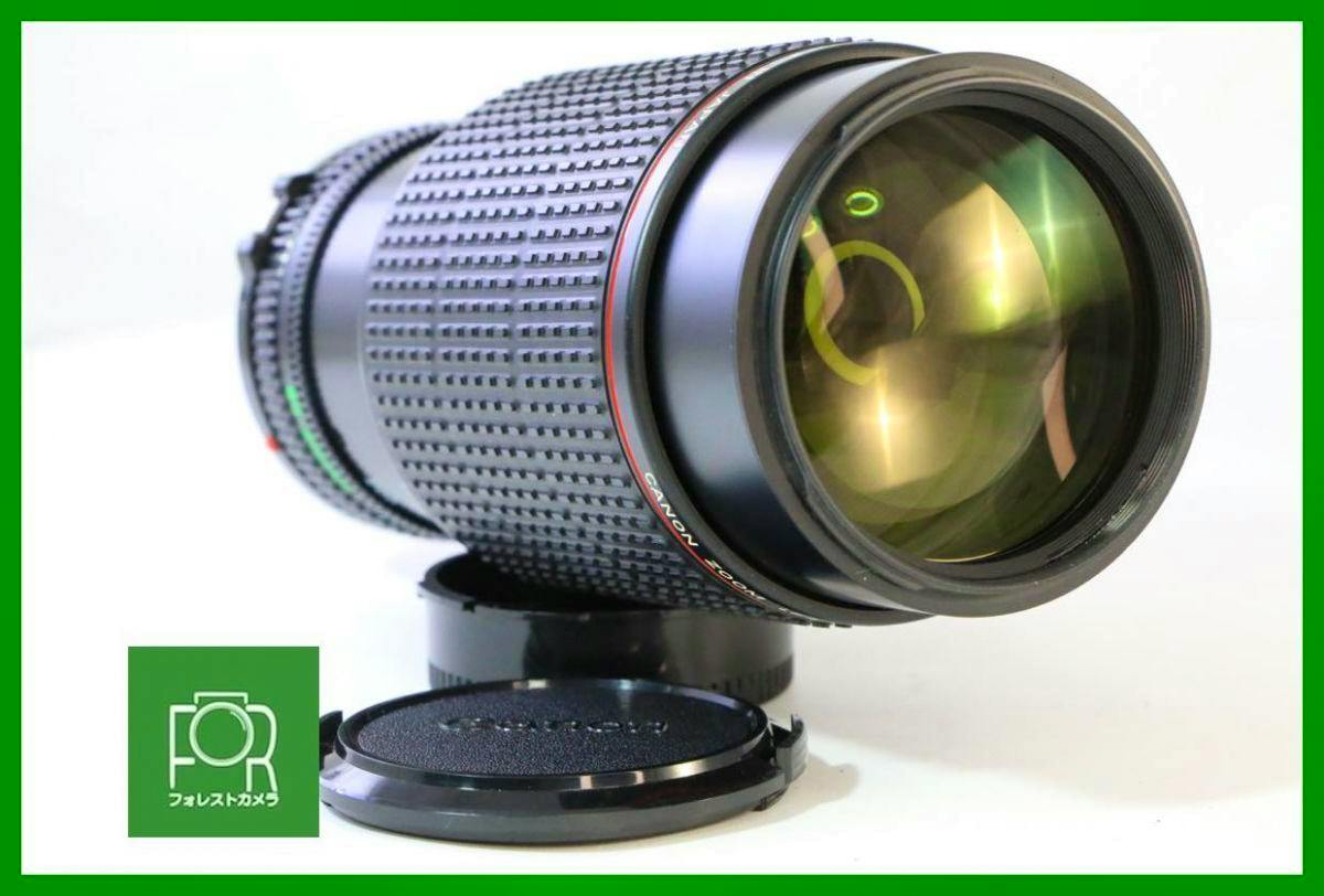 Angled view of the Canon New FD 80-200mm F4 L camera lens showing the front glass element, textured barrel, and a front lens cap.