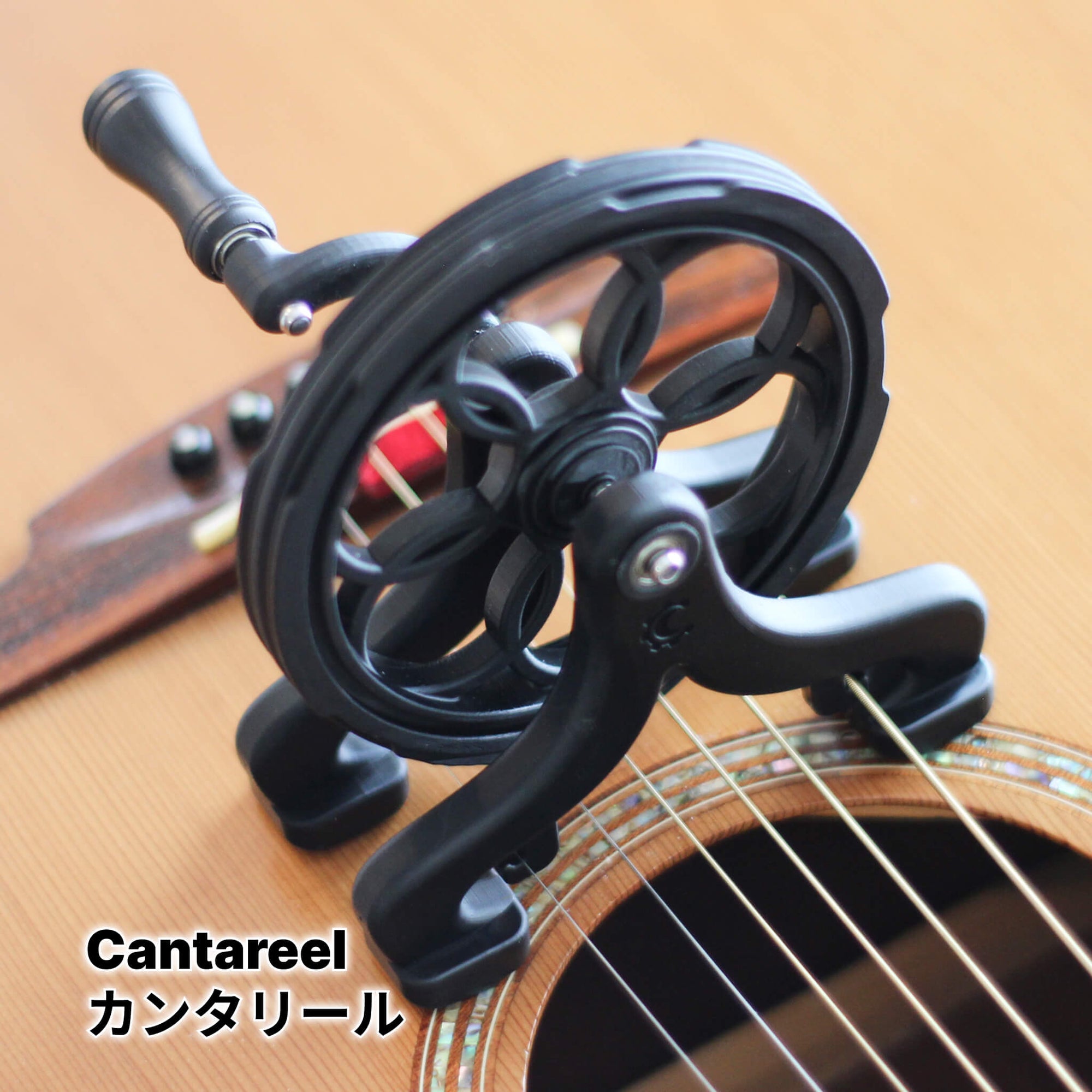 Crank-driven rotating guitar attachment (Cantareel) clamped over an acoustic guitar's soundhole, showing the wheel and handle.
