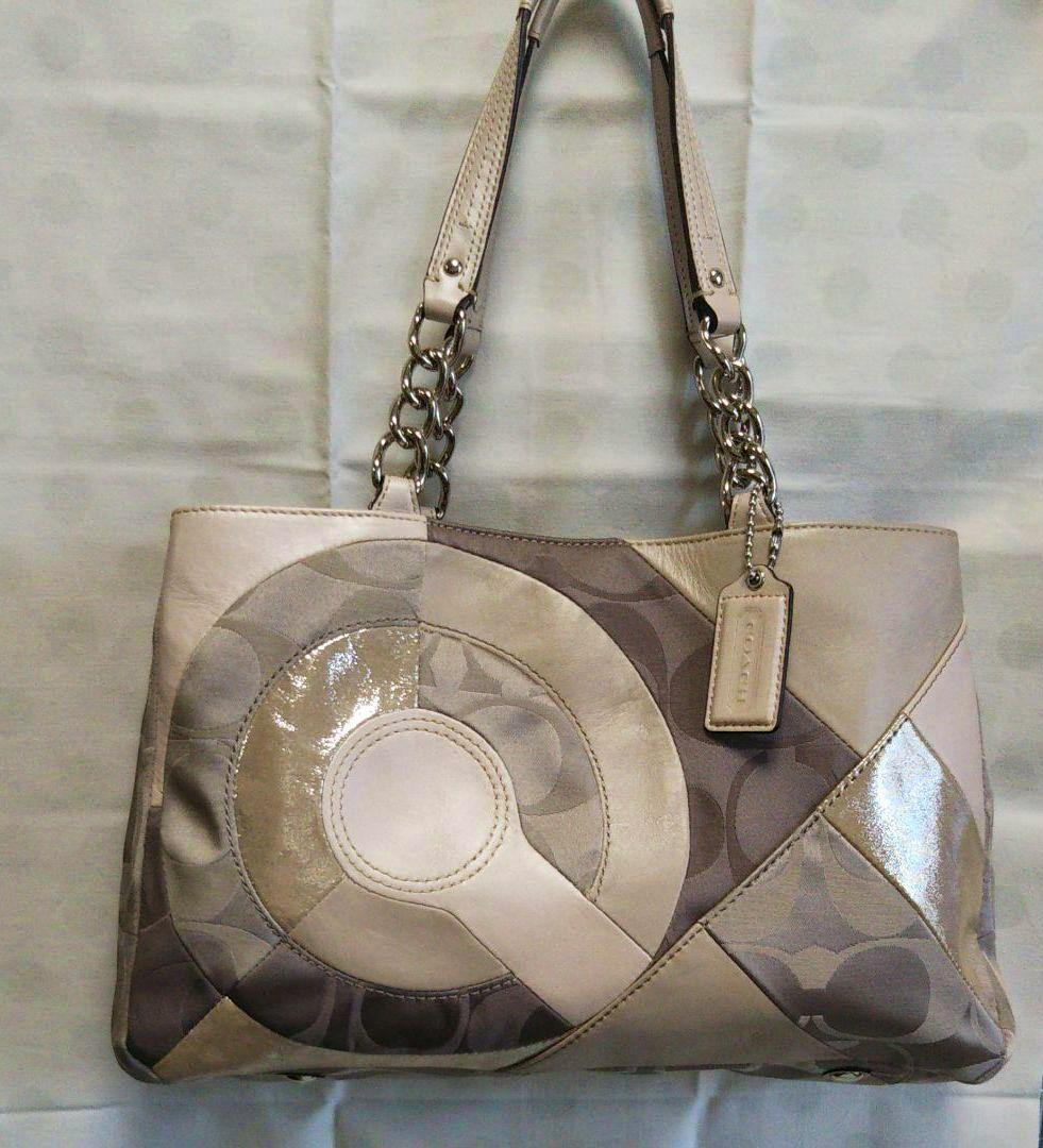 Front view of a beige canvas shoulder bag featuring a circular patchwork design and chain-link shoulder straps.