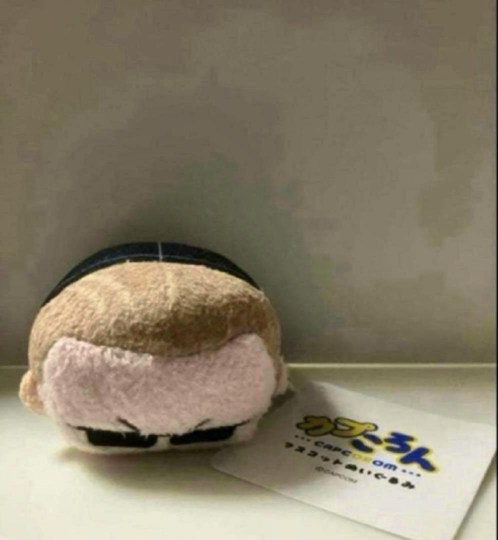 Frontal photo of the カプころん Albert Wesker plush toy resting on a surface with its tag visible.