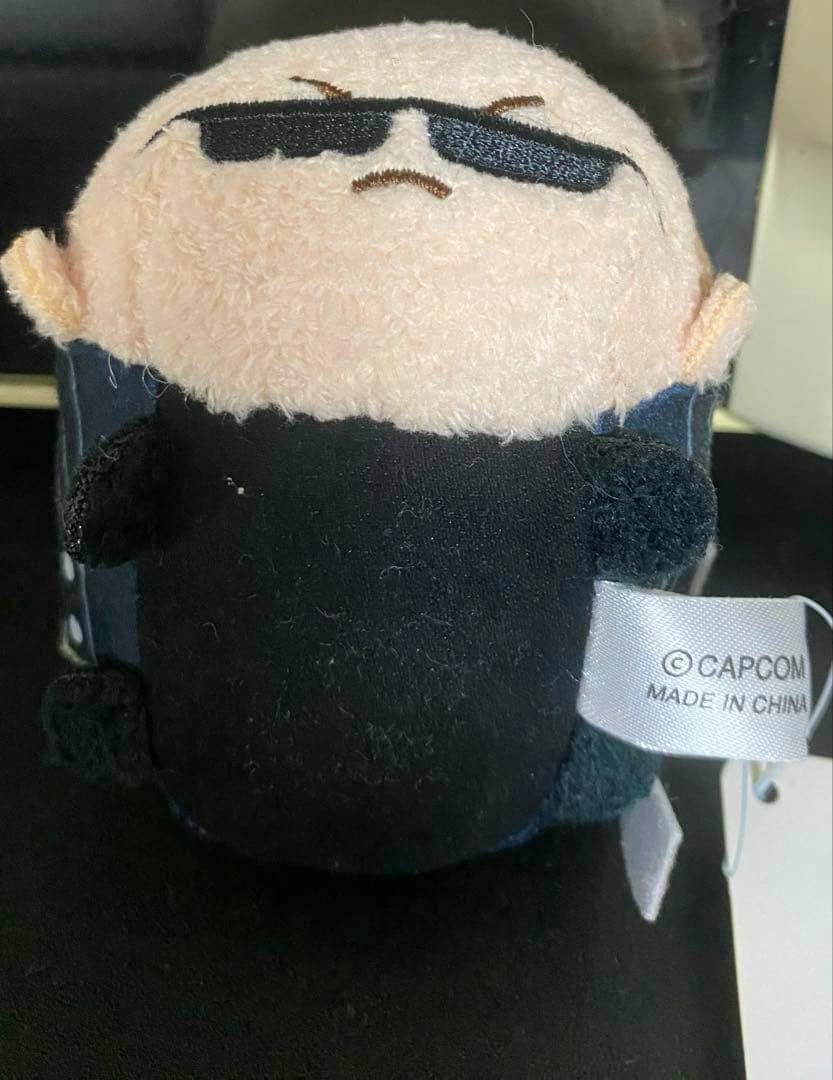 Front view of the plush toy showing a character with embroidered sunglasses, a black outfit, and a CAPCOM tag.