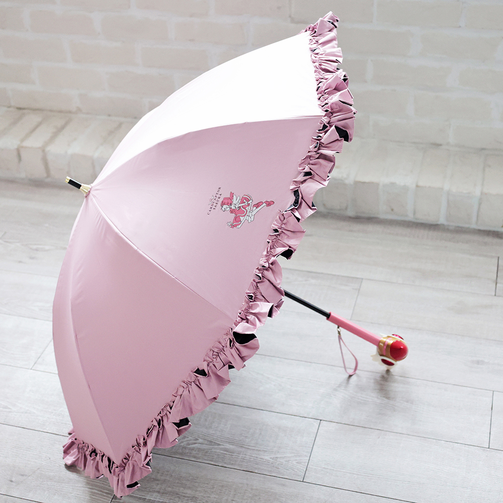 Pink Cardcaptor Sakura long umbrella with ruffled edges and a printed motif, shown open on the floor with the wand-style handle visible.