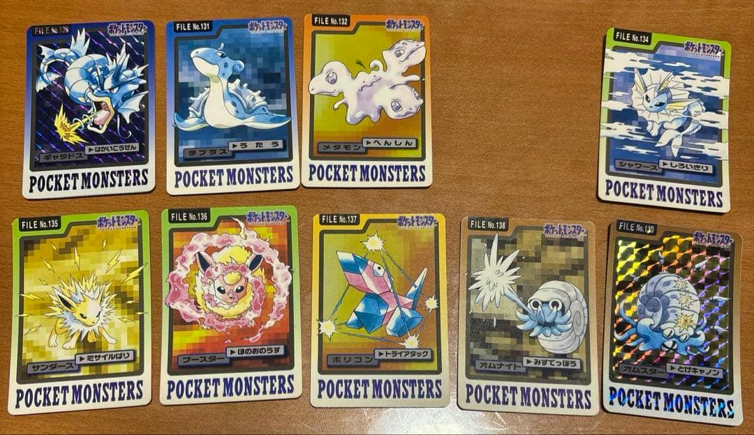 Several Pocket Monsters photocards (cards numbered 130–139 with 133 missing) laid out on a wooden surface, showing various Pokémon designs.