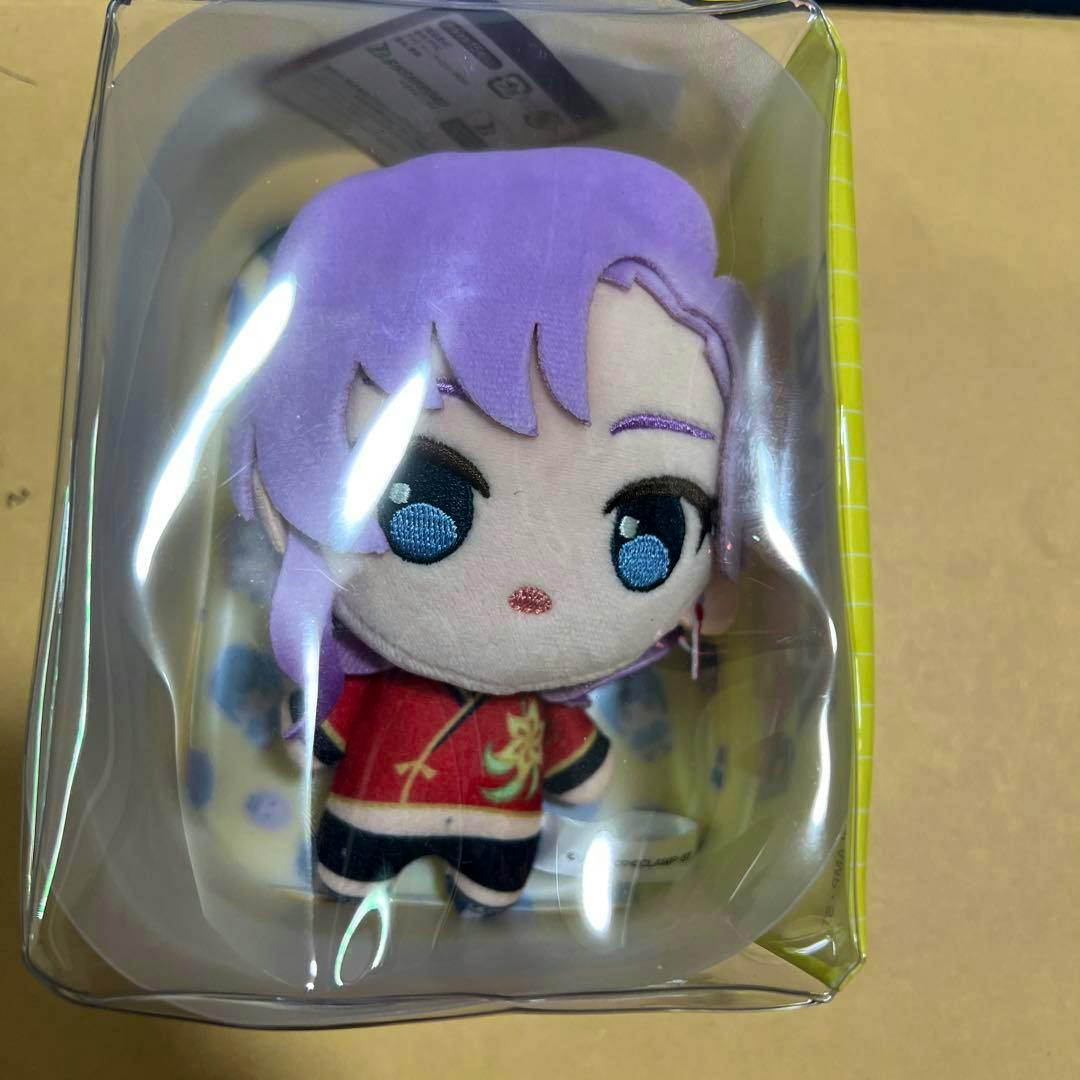 A small purple-haired chibi plushie in clear plastic packaging wearing a red outfit.