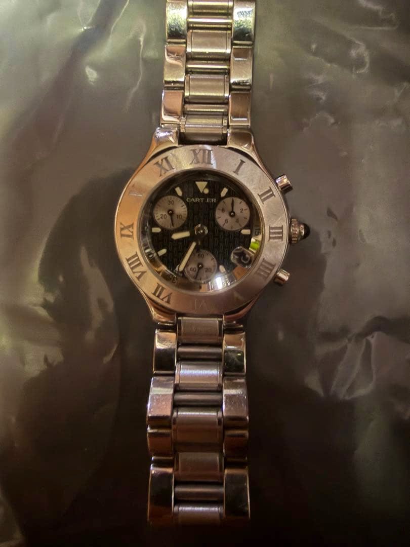 Top-down photo of the Cartier wristwatch with a black dial and metal bracelet laid on a dark surface.