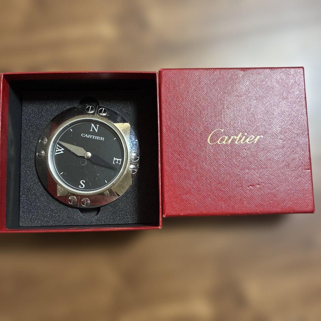 A Cartier compass ornament with a black dial displayed inside an open red Cartier box.