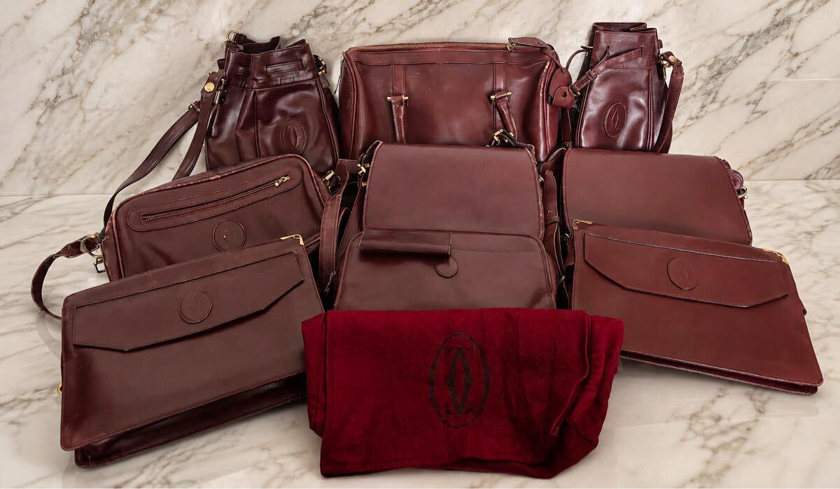 Several burgundy Cartier leather bags and a matching burgundy dust bag arranged on a marble surface.