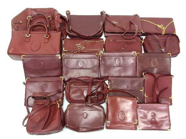 Top-down photo of multiple burgundy Cartier Must Line leather handbags and shoulder bags arranged together.