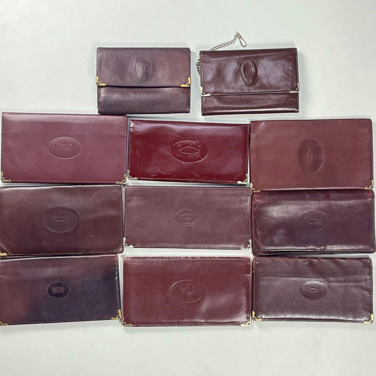 Eleven burgundy Cartier long wallets arranged flat on a light background, showing exterior fronts and embossed logos.