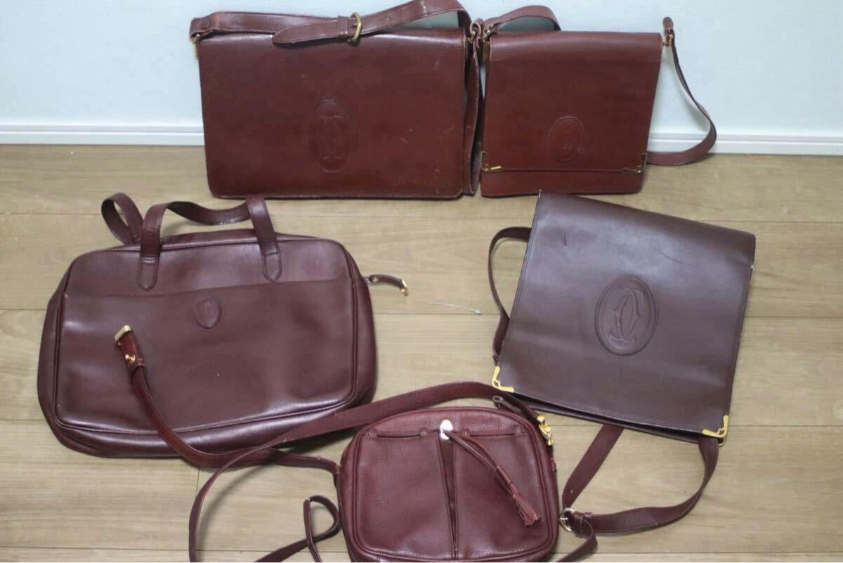 Five burgundy Cartier leather bags in different shoulder and hand styles arranged on a wooden floor.