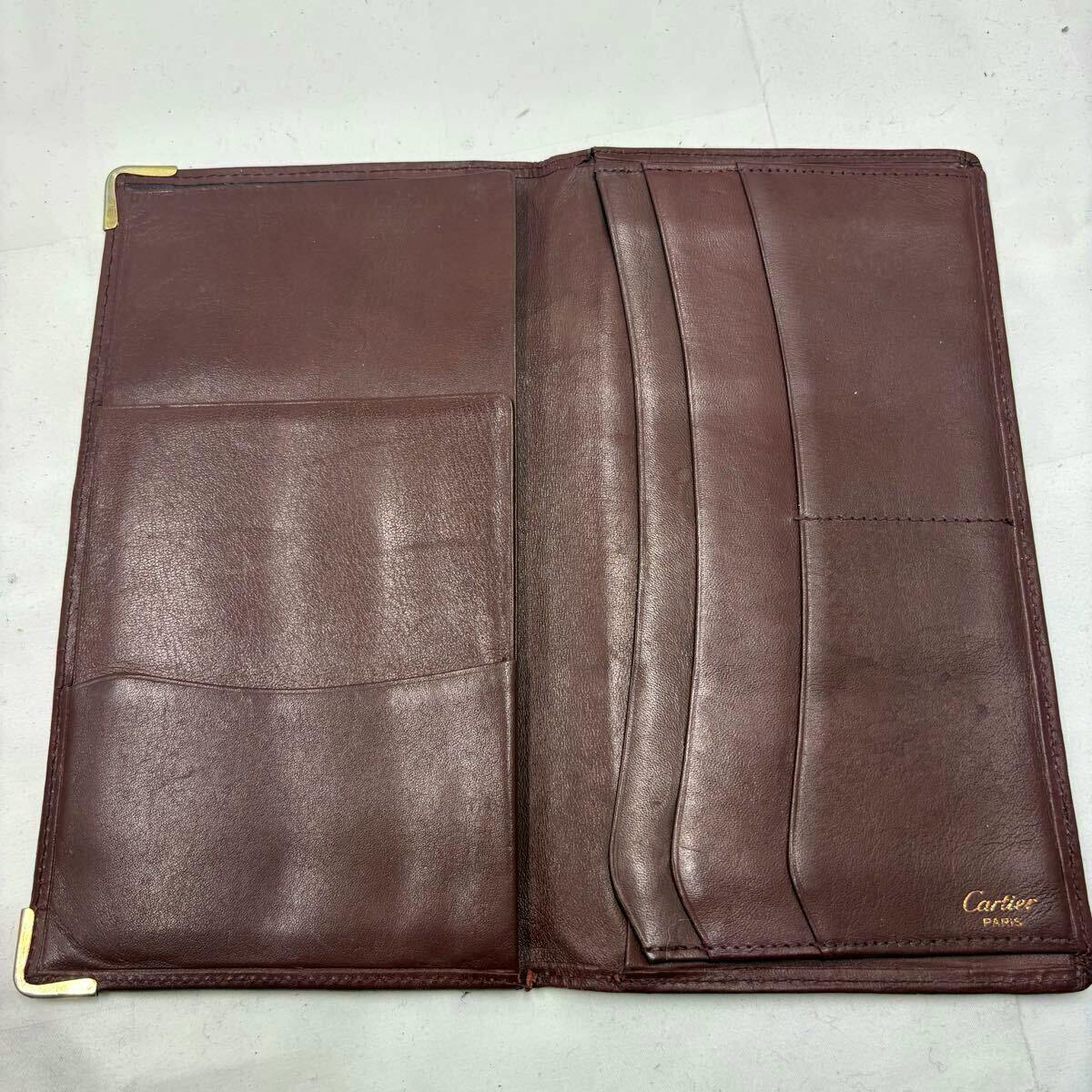 Open burgundy Cartier long wallet showing interior card slots, bill compartment, and a gold "Cartier Paris" mark.