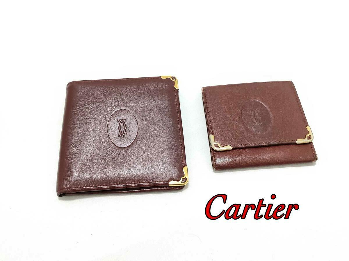 Two bordeaux Cartier leather wallets (a bi-fold and a coin case) with gold corner hardware on a white background.