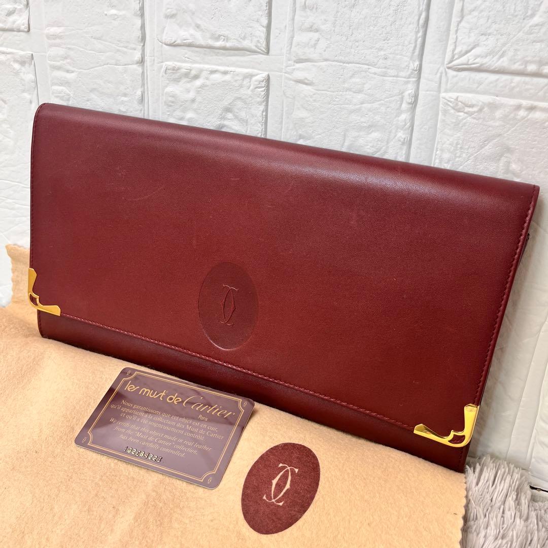 Burgundy Cartier Must Line leather clutch bag with gold corner hardware displayed with its authenticity card and dust cloth.