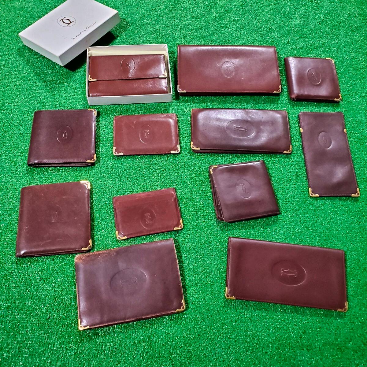 Several burgundy Cartier wallets and a Cartier box arranged on green turf.