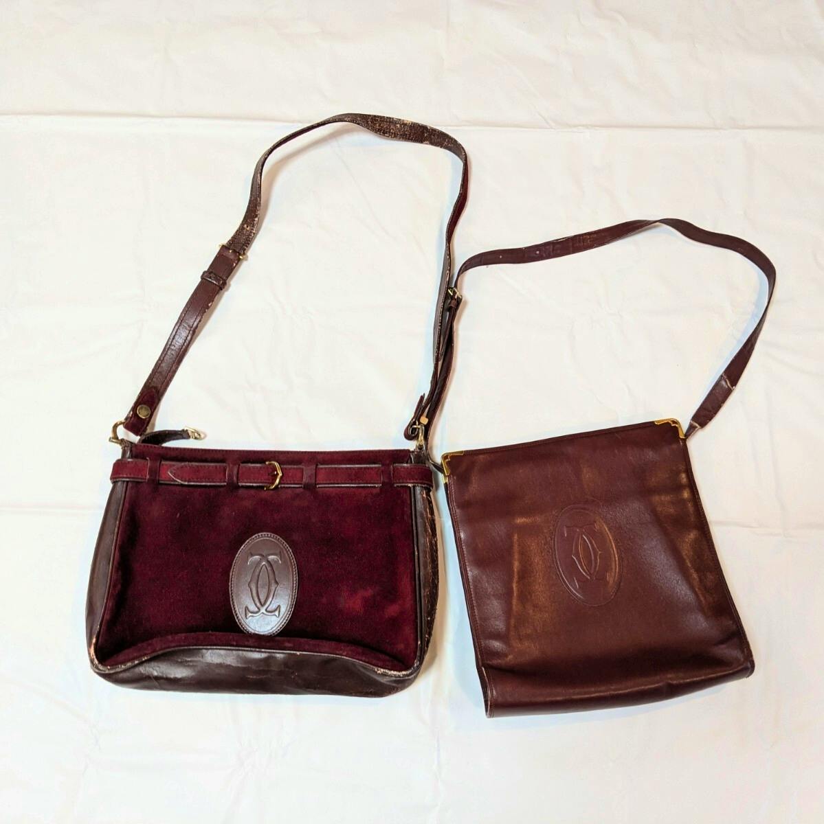 Two burgundy Cartier shoulder bags laid flat on a white background, showing straps and front embossed logos.