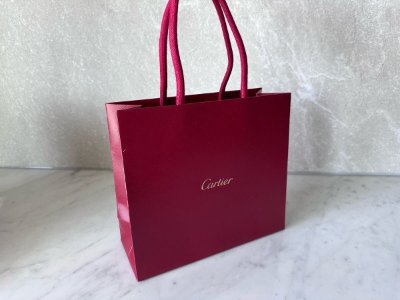 Red Cartier paper shopping bag with rope handles and Cartier logo on the front.
