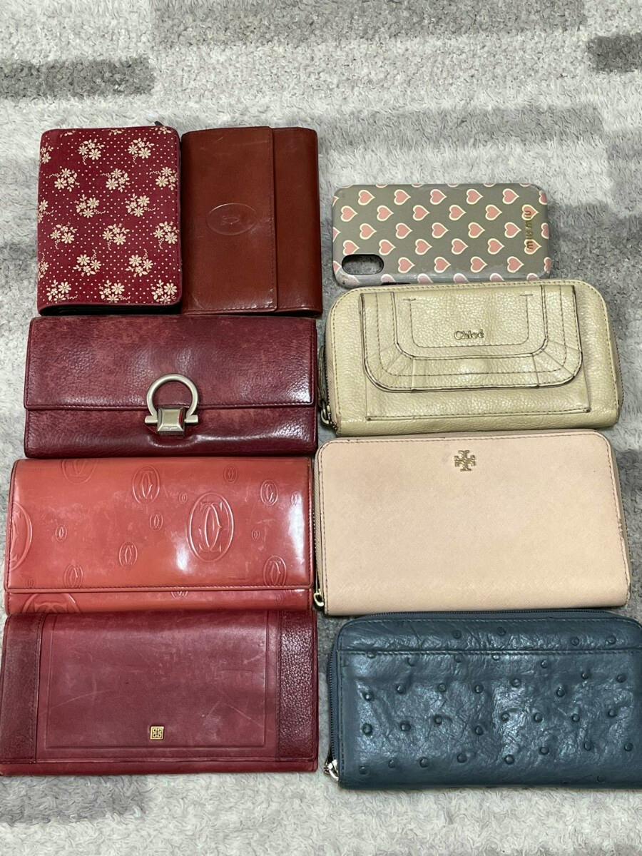 Nine wallets of different colors and styles arranged on a gray carpeted surface.