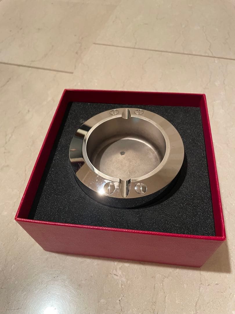 Cartier stainless steel ashtray in its red presentation box on a tiled floor.