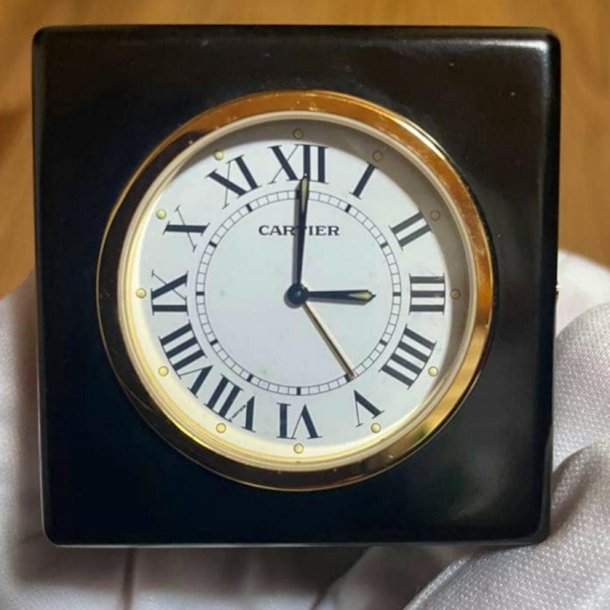 Front view of a Cartier black-and-gold table clock showing a white dial with Roman numerals and the CARTIER logo.