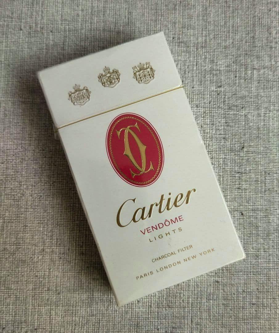 A white Cartier Vendôme Lights cigarette pack with red and gold logo photographed on a textured fabric background.
