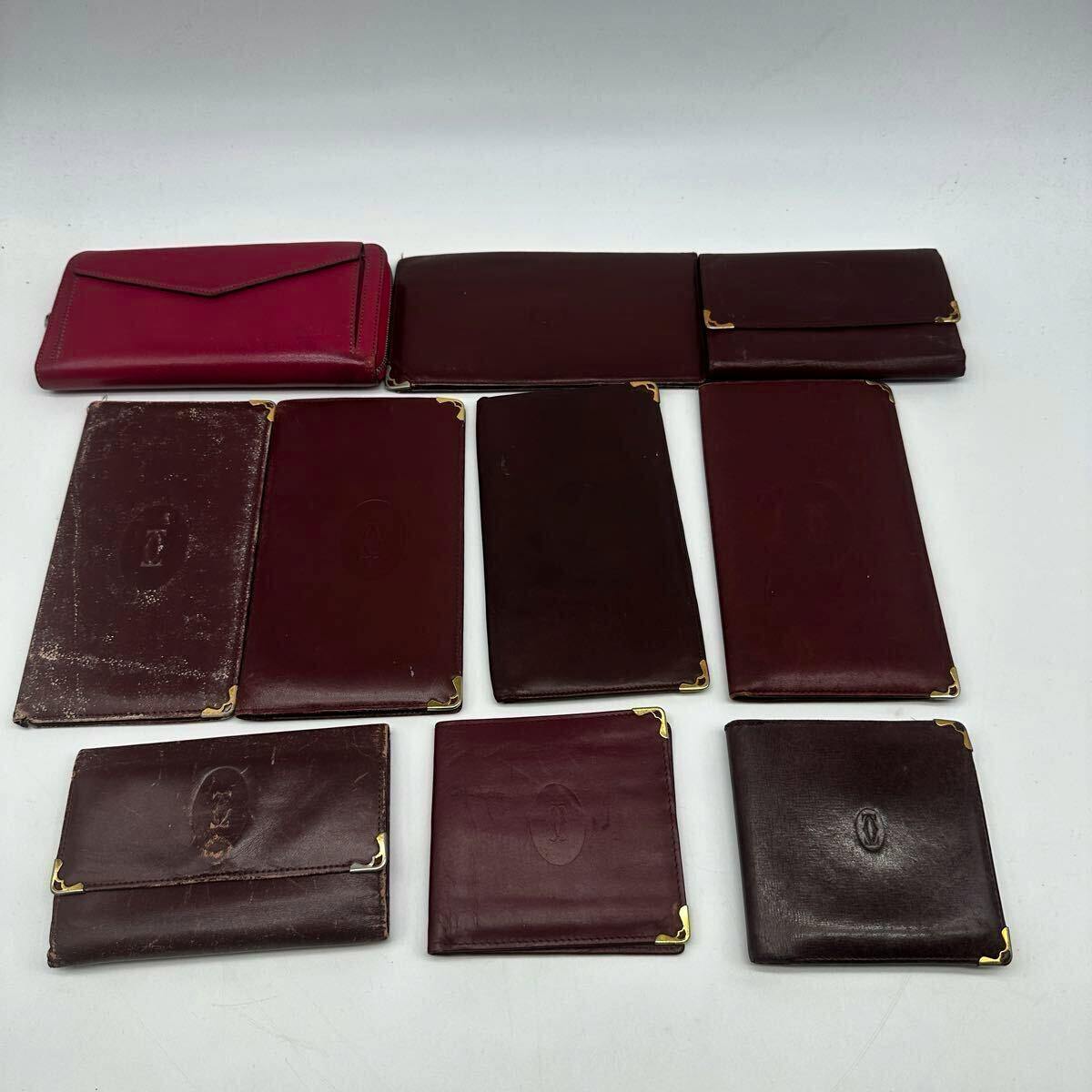 Ten Cartier leather wallets and small purses arranged on a white background, mostly burgundy and brown with gold corner accents.