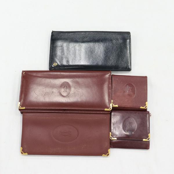 Five wallets made of leather — four brown and one black — arranged flat on a white background.